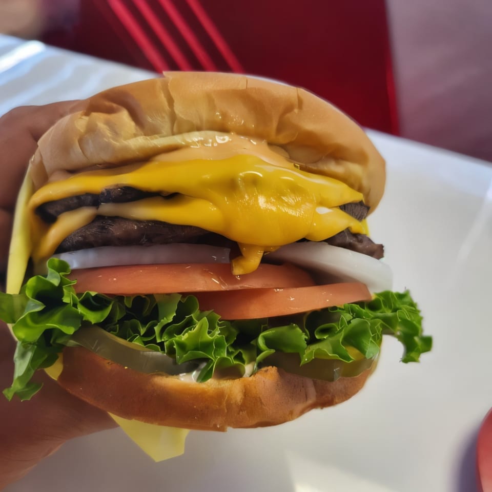 A hand holds a Burger Time double cheeseburger with melted cheese, lettuce, tomato, onion, and pickles.