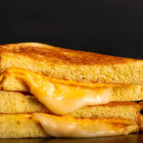 A grilled cheese sandwich with melted yellow and white cheese oozing out, against a dark background.